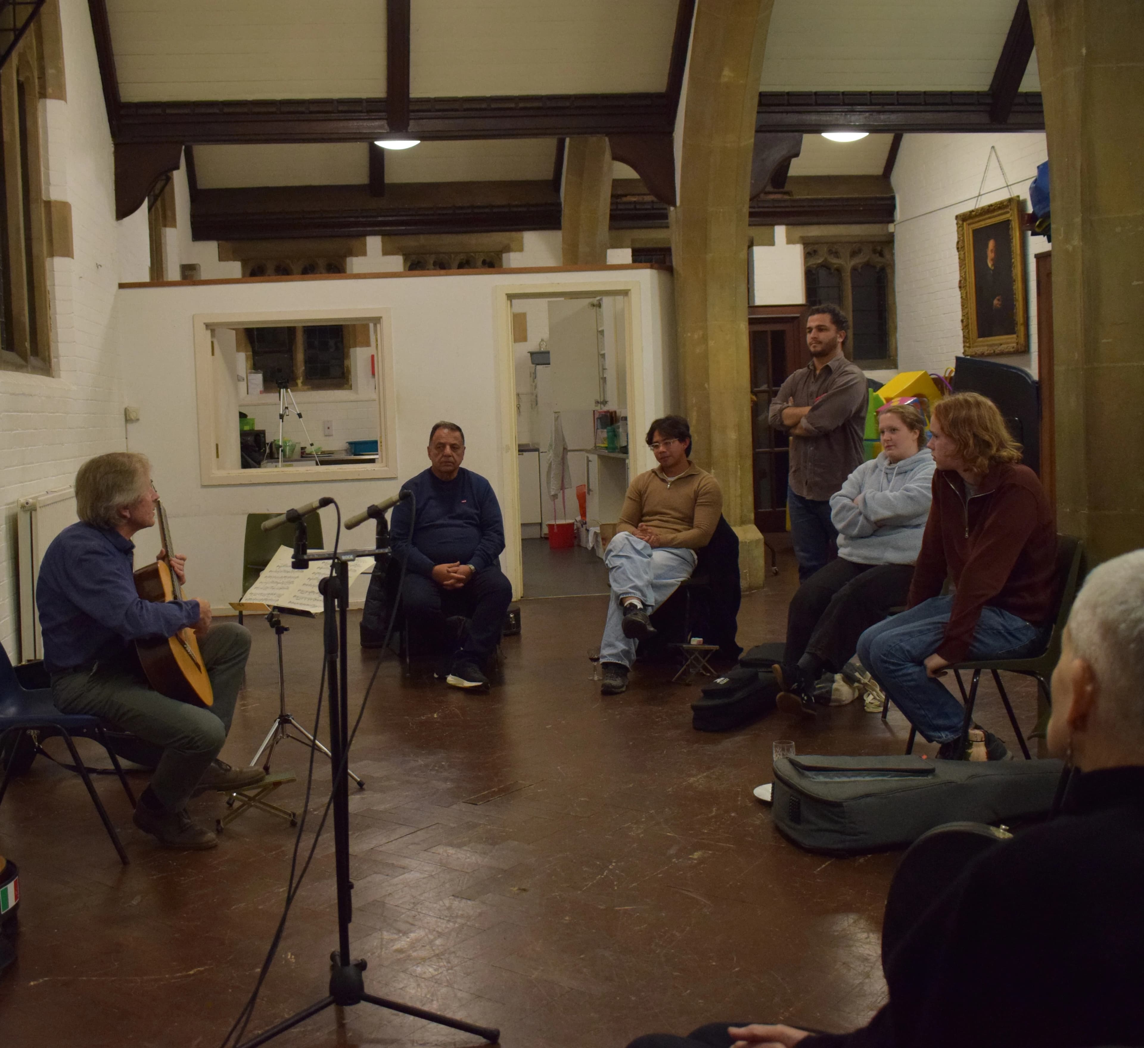 A guitarist performing to members of the society in a church hall